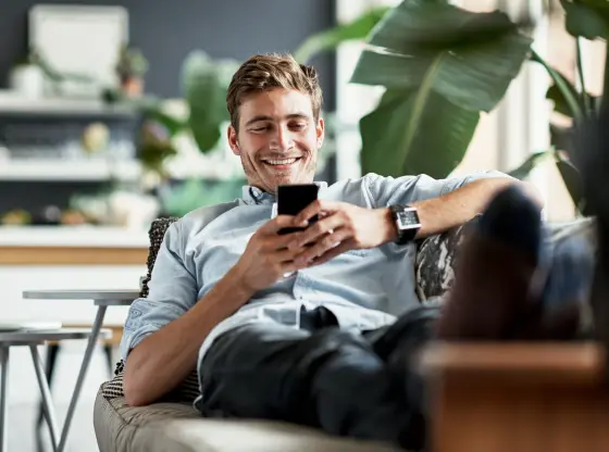 Mann liegt gemütlich mit Handy in der Hand auf dem Sofa und aktualisiert bequem seine Daten